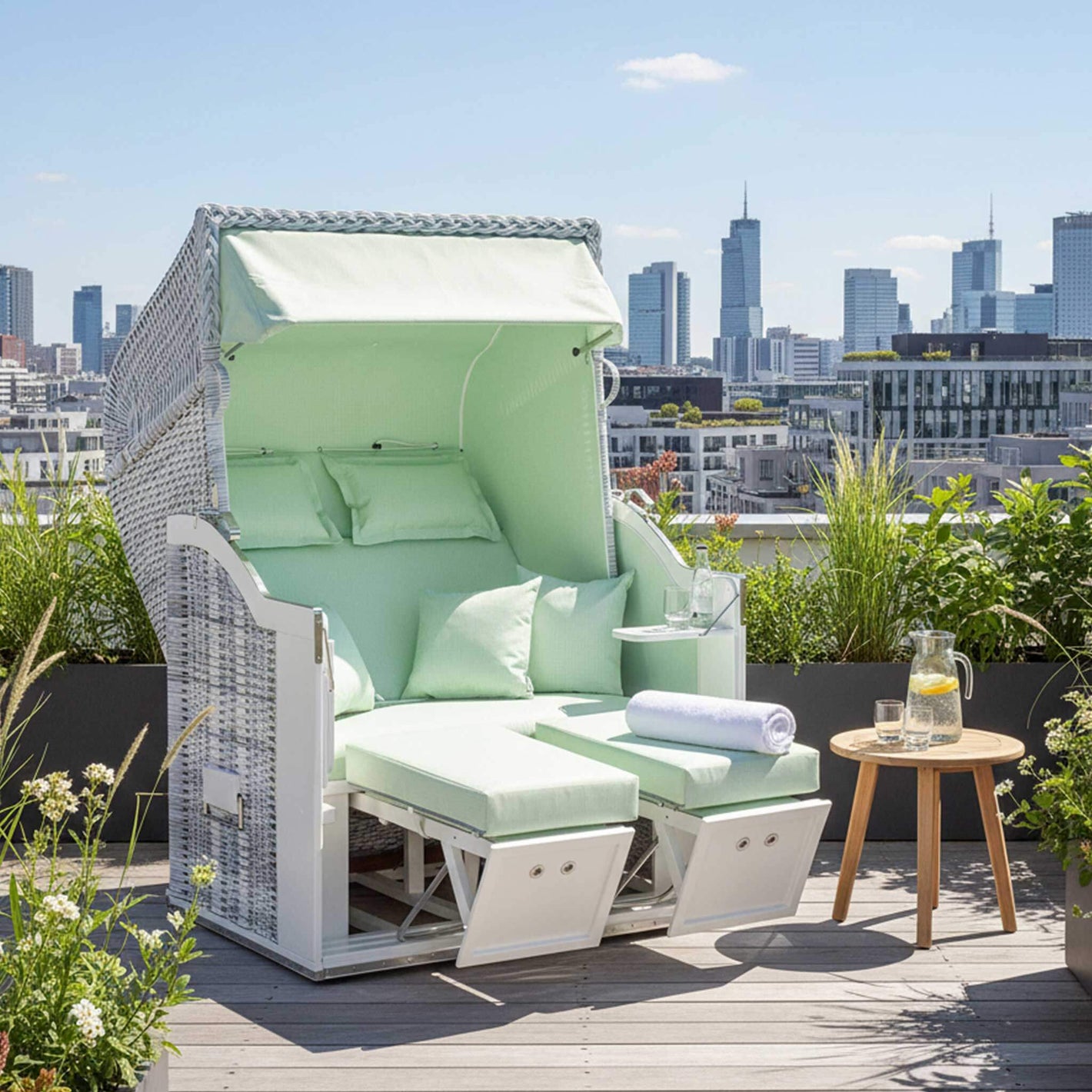 Strandkorb Classic 2-Sitzer white-washed mit hellgrünen Kissen auf einer Dachterrasse mit Stadtansicht.