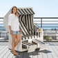 Strandkorb Sonnenpartner Classic weiss mit grau-weißen Streifen, Frau stehend daneben auf Terrasse mit Meerblick